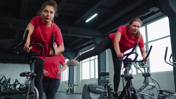 Group Athletic Girls Performing Aerobic Riding Training Exercises on Cycling Stationary Bike in Gym alt