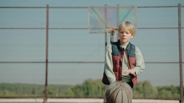 Kid Hitting a Basketball Ball Practicing on a Court in the Park alt