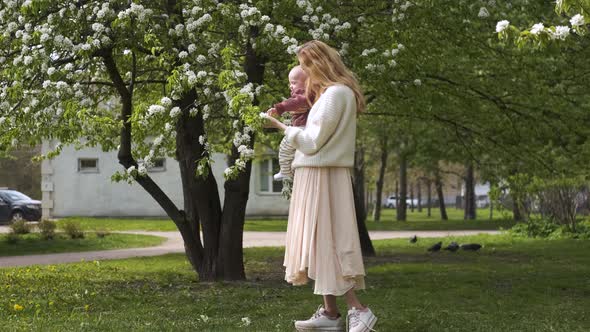 beautiful woman with a child in her arms is looking at a blooming tree