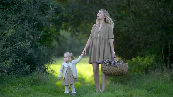 Happy young mum and daughter with wild flowers bouquet walking together outdoor