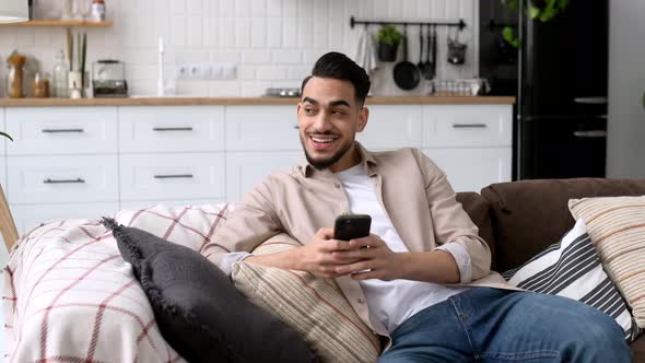 Attractive Indian or Arabian Young Man Sit in a Modern Living Room on Comfortable Sofa Uses His alt