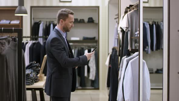 A Side View Slow Motion Panoramic Shot of a Dark Haired Man in a Clothing Shop Walking Up To a