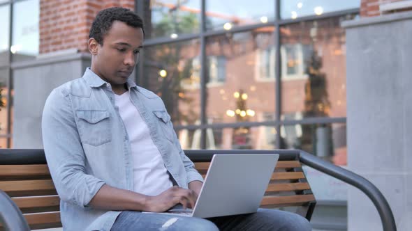 African Man working on Laptop, Sitting on Bench alt