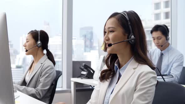 Asian woman customer service operators talking on headsets and using computer at call center