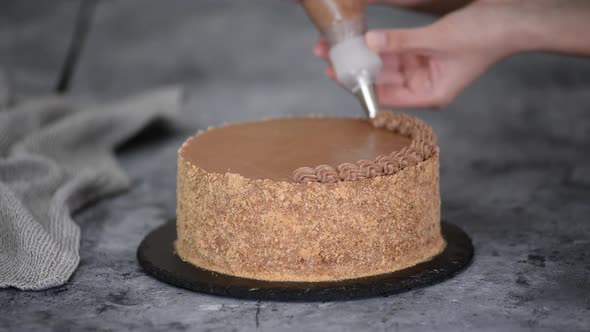 Female Hands Decorate a Cake with Chocolate Cream From a Pastry Bag with a Nozzle