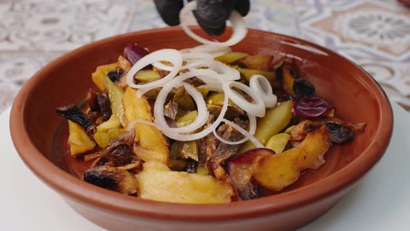 Fried Potatoes with Mushrooms and Onion Rings in Clay Plate Spinning Round on Table