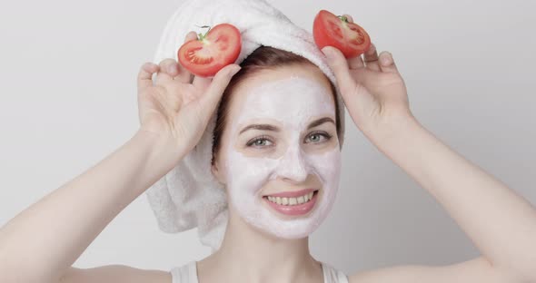 Pretty Woman with Towel on Head and Facial Mask Having Fun Smiling and Holding Two Pieces of Tomato alt