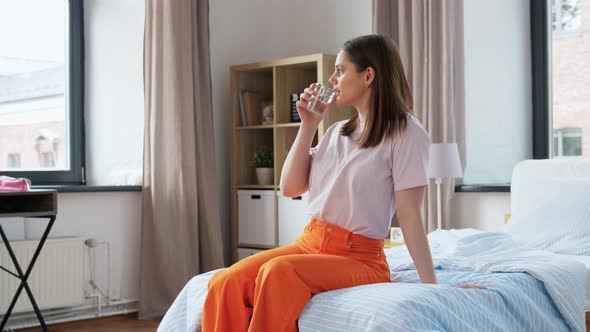 Girl with Glass of Water Sitting on Bed at Home