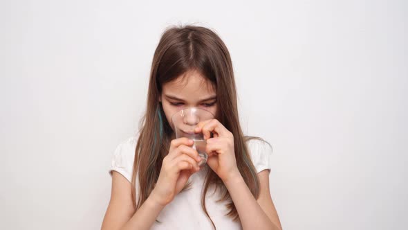A Teen Girl Puts a Pill in Her Mouth and Wash Down with Water Against White Wall