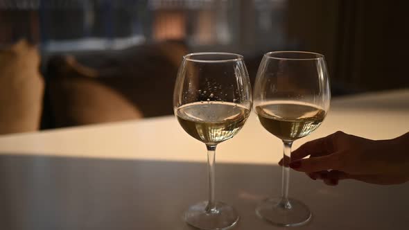 Female Hand Taking One of Two Glasses with Dry White Wine on White Table