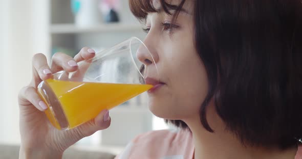 Young pretty woman drinking orange juice while looking on TV alt