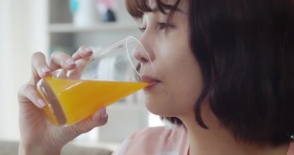 Young pretty woman drinking orange juice while looking on TV