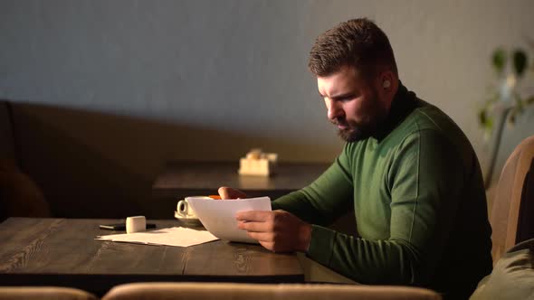 Bearded Hipster Signs Papers Sitting in a Cafe