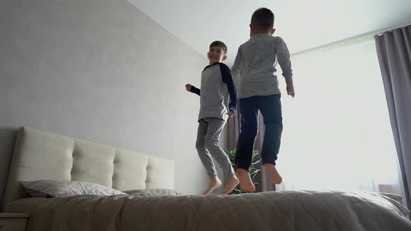 Two Little Brothers in Pajamas Cheerfully Jumping on Big Bed