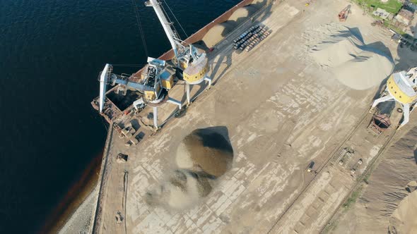 Working Crane Unloads a Barge with Rubble on Water at Port. alt