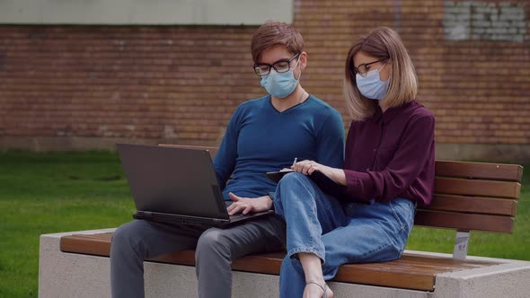 Two professional coworkers in protective mask discuss concentrating typing on laptop alt