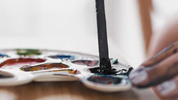 Artist Mixes Blue Paint in Cup of White Palette at Easel alt