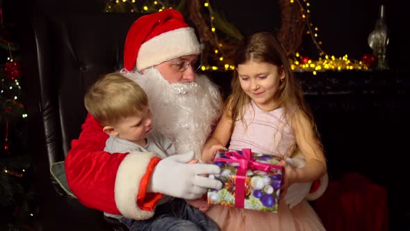 Little boy and girl sitting on the lap of Santa Claus. Christmas present.