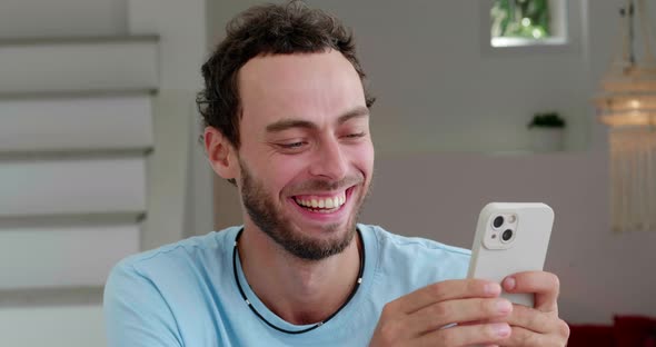 Handsome Serene Caucasian Young Man Having Fun at Home Using His Smartphone Scrolling News Feed and alt
