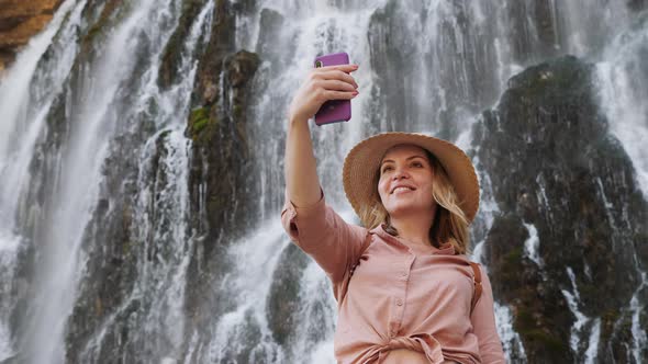 Woman Taking a Selfie on the Background of a Waterfall alt