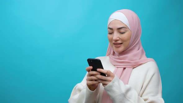 Stylish Happy Young Muslim Woman Typing Message on Mobile Phone and Smiling Chatting Having Online