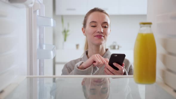 Online ordering of goods from the supermarket. Woman in bathrobe looks into an empty refrigerator