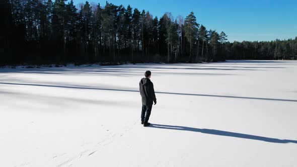 A young guy in dark clothes with short hair walks on an icy lake