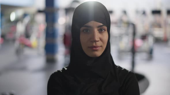 Portrait of Gorgeous Young Beautiful Middle Eastern Woman in Hijab Turning to Camera Standing in Gym alt