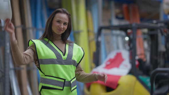 Young Canadian Warehouse Worker Taking Off Hard Hat Touching Hair Looking at Camera Smiling alt