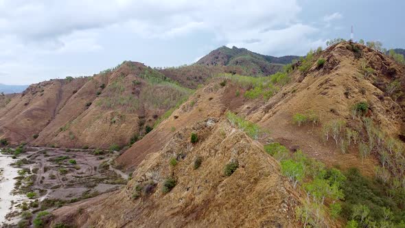 Aerial drone rising over dry season brown hill landscape with a telecommunications tower on top on t alt