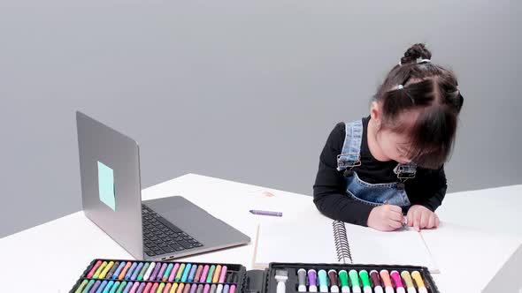 Girl drawing with wax gis in notebook with blank leaves. Showing your camera drawing. alt