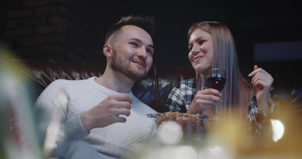 Happy Millennial Couple Sitting on Couch Having Fun Watching TV Show at Home in Evening
