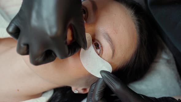 Eyelash Extension Master Sticks a Protective Patch Under the Eyes of a Beautiful Young Woman alt