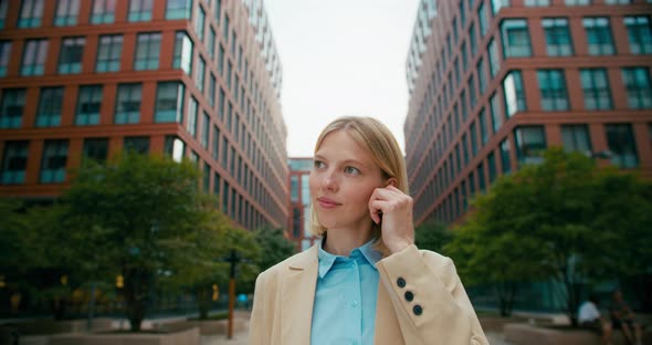 A Female Office Worker Talking on the Phone Through Wireless Headphones alt
