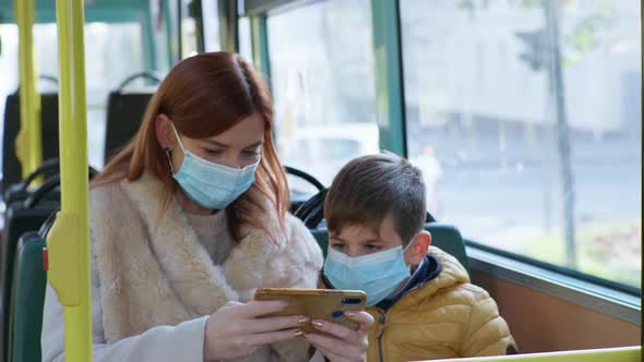 Female Parent with Boy Wearing Medical Masks To Protect Against Virus and Infection Play Games on