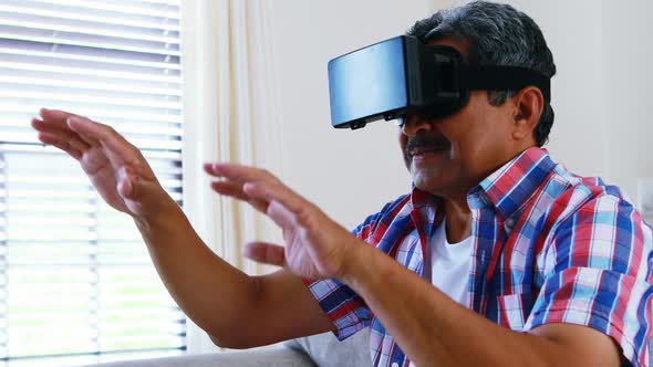 Senior man using virtual reality headset in living room 4k alt