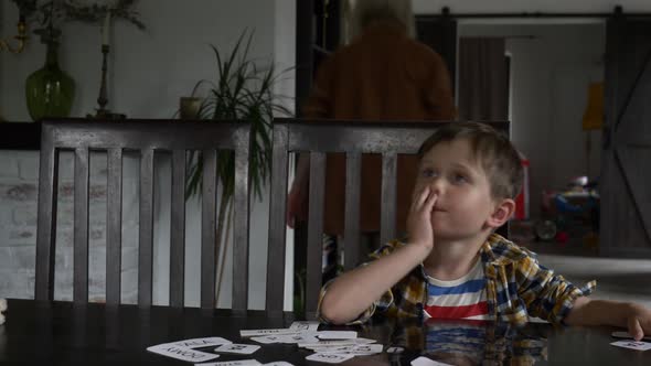 boy sits and learning how to speak words by the cards at home at the table