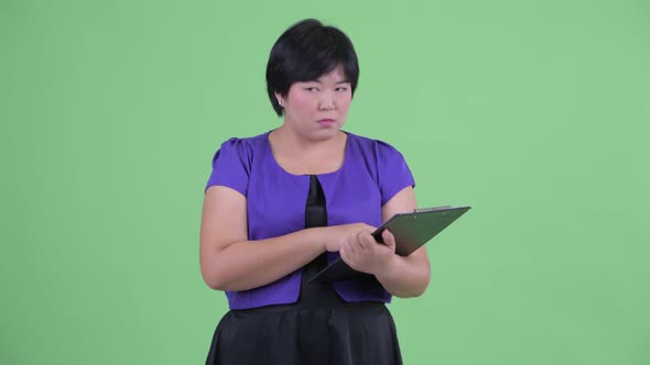 Young Beautiful Overweight Asian Woman Holding Clipboard and Directing alt