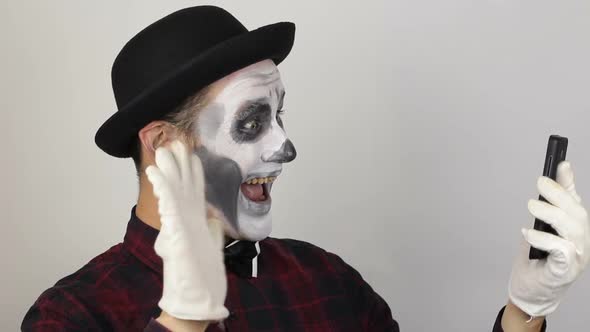 A Terrible Man in Clown Makeup and Video Chat. The Scary Clown Communicates with Friends Via Video