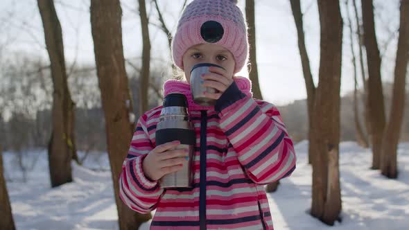 Portrait of Cute Smiling Child Girl Kid Traveler Walking Drinking Hot Drink Tea in Winter Park alt