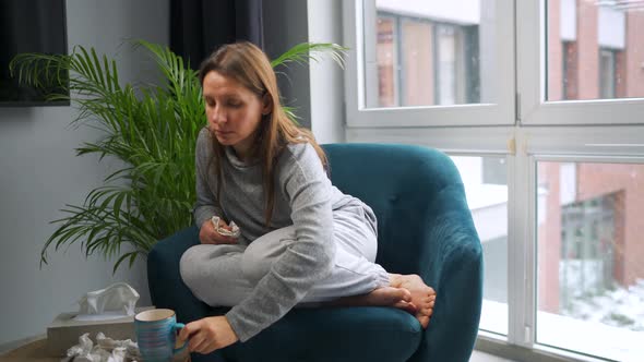 Unhealthy Woman Sits in a Chair Drinks Hot Tea or a Cold Medicine and Sneezes or Blows Her Nose Into alt