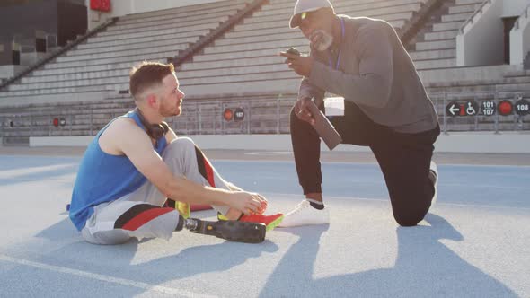 Diverse male coach and disabled athlete with prosthetic leg talking during training session alt
