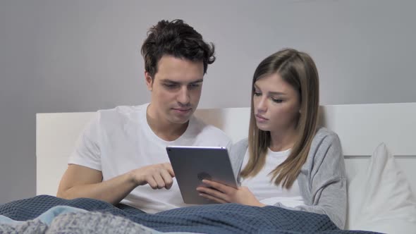 Relaxing Young Couple Browsing Internet on Tablet in Bed alt