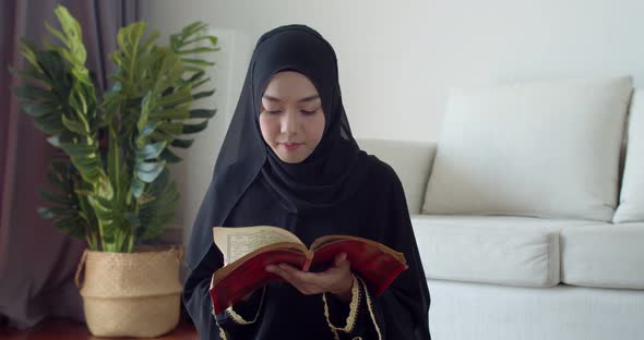 Young Muslim woman wearing traditional clothing and hijab reading Quran