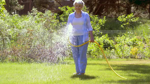 Senior Woman Watering Lawn By Hose at Garden 35 alt