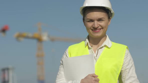 Girl Builder in Protective Clothes at Construction Site. Girl Holds a Folder with Documents and alt