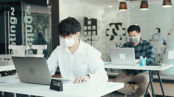 Asian colleague works while wearing a mask in the office during COVID-19.