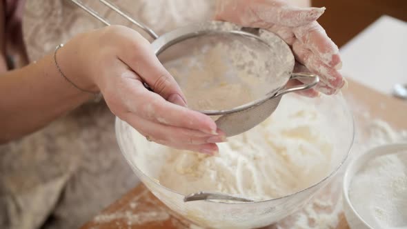 Top View of Female Baker Sifting Flour with Sieve in Big Glass Bowl for Making Dough alt