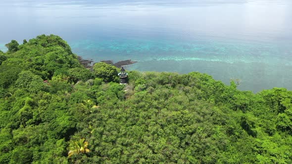 Rotating aerial shot of a lighthouse on a tree covered mountain on an island off Madagascar alt