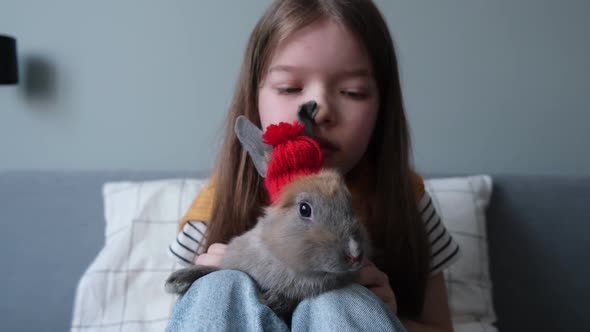 a Little Girl Holds a Rabbit in a Hat in Her Arms Strokes It Plays with It